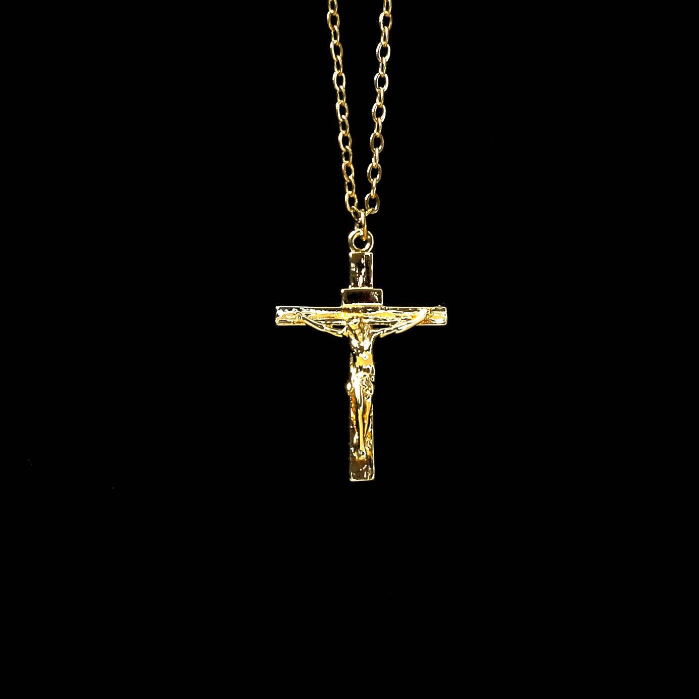 Pendentif croix Jésus en acier inoxydable doré suspendu à une chaîne fine, affiché sur un fond noir minimaliste.