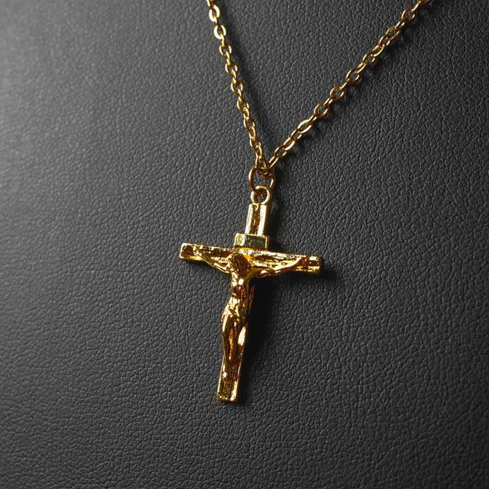 Chaîne pendentif croix en acier inoxydable doré avec Jésus crucifié, affiché sur un fond en cuir noir pour une finition raffinée.