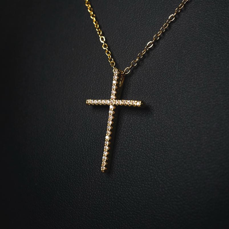 Collier croix en acier inoxydable doré avec incrustations de pierres brillantes, suspendu à une chaîne fine élégante.