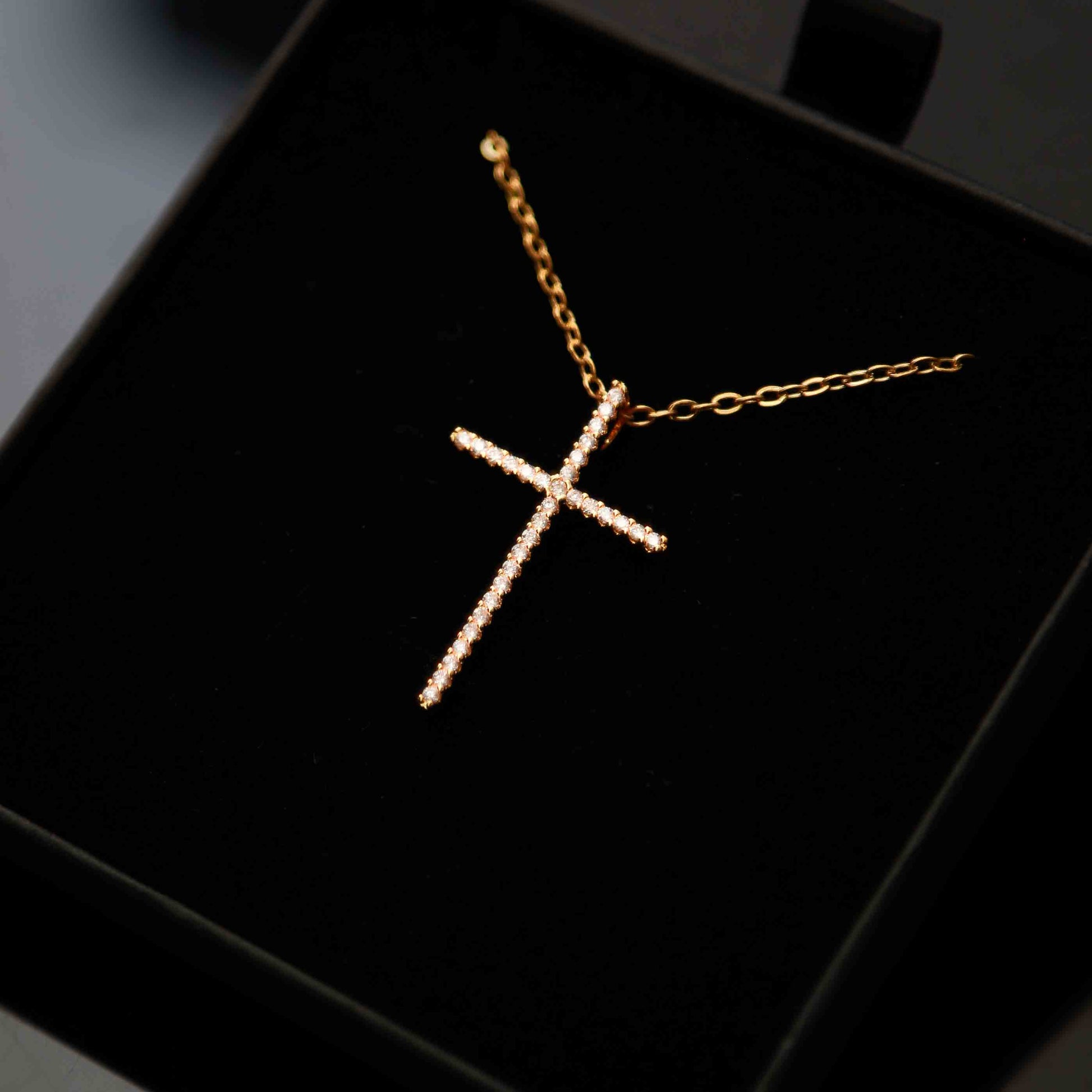 Pendentif croix en acier inoxydable doré avec pierres scintillantes, présenté dans un écrin noir raffiné.