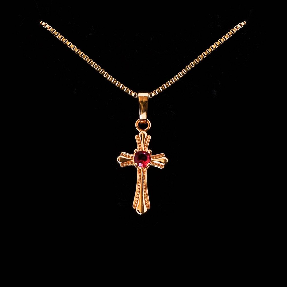 Collier croix doré avec pierre rouge centrale et détails gravés, suspendu à une chaîne fine en acier inoxydable.