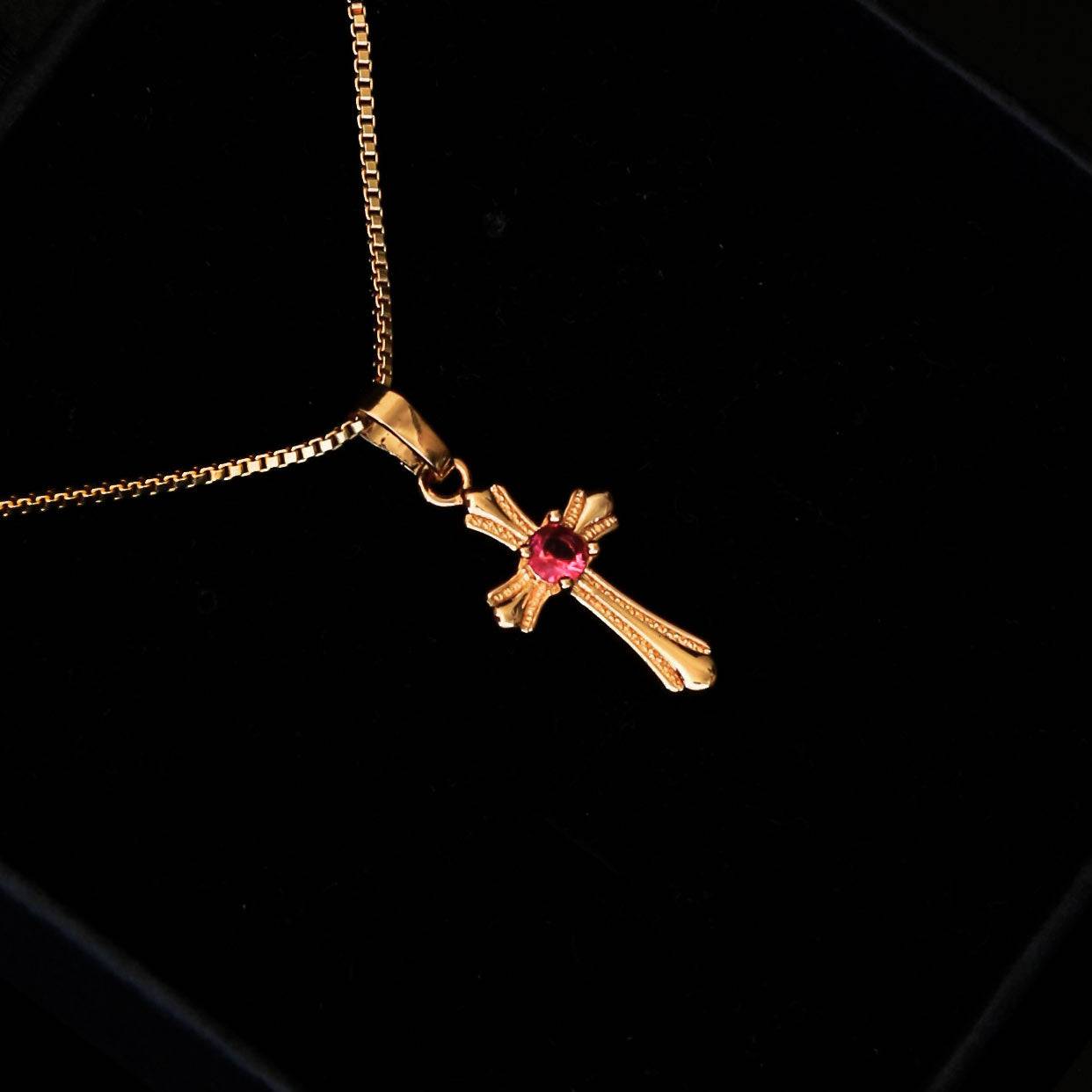 Collier croix doré avec pierre rouge centrale, design raffiné en acier inoxydable, idéal pour un cadeau religieux.