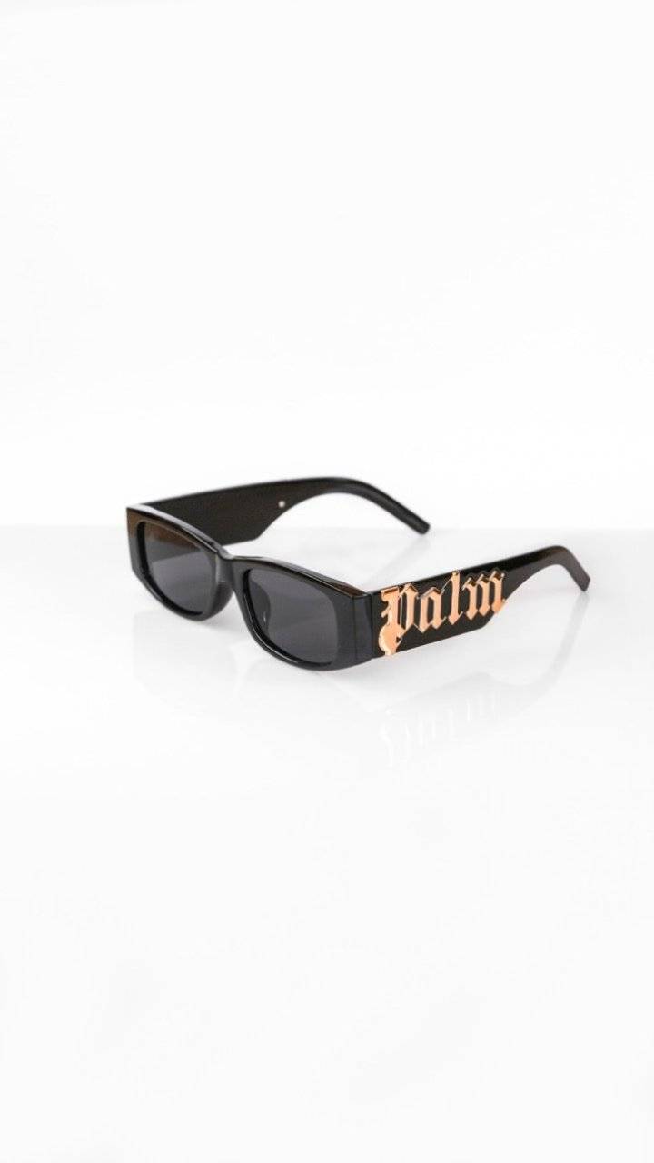 Lunettes Palm/Angels avec verres noirs et logo 'Palm' doré sur les branches. Style audacieux et protection solaire élégante.