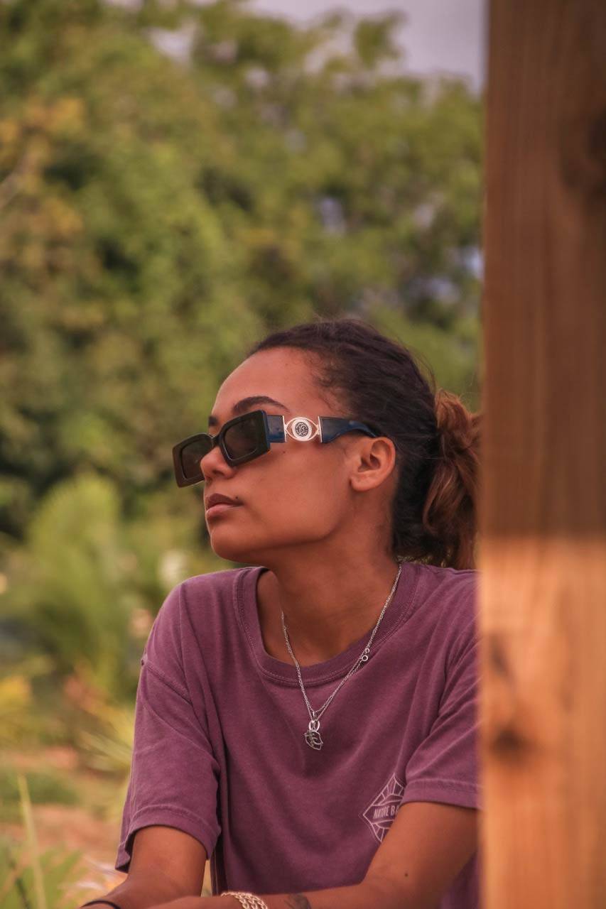 Homme portant des lunettes monture carrée noires avec détails dorés, soulignant un style décontracté et élégant en plein air.
